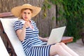 Hey you! Portrait of angry serious young adult freelancer woman in hat and dress sitting on cozy daybed with laptop and pointing Royalty Free Stock Photo