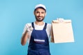 Hey you! Portrait of cheerful bearded handyman in overalls and gloves carrying parcel, pointing to camera Royalty Free Stock Photo