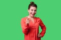 Hey you! Portrait of lovely positive young woman with bun hairstyle, big earrings and in red blouse. isolated on green background Royalty Free Stock Photo