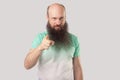 Hey you! Portrait of serious middle aged bald man with long beard in light green t-shirt standing, pointing and looking at camera Royalty Free Stock Photo