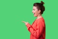 Hey you! Side view portrait of happy girl with bun hairstyle, big earrings and in red blouse. indoor studio shot isolated on green