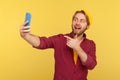 Hey you there! Friendly hipster guy in checkered shirt pointing finger to cellphone, smiling talking video call on mobile phone Royalty Free Stock Photo