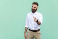 Hey you! Young adult bearded man, pointing finger and looking at camera. On light green background. Indoor Royalty Free Stock Photo