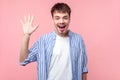 Hi, Hello! Portrait of happy friendly brown-haired man waving hand to camera. isolated on pink background