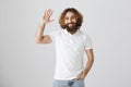 Hi, my friend. Portrait of good-looking ordinary eastern male with curly hair and beard raising hand and waving in