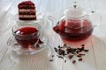 Hibiscus tea in cup and teapot, tea leaves, piece of red velvet cake on white wooden background. Royalty Free Stock Photo