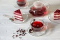 Hibiscus tea in cups and teapot, tea leaves, for dessert red velvet cake pieces on white wooden background. Royalty Free Stock Photo