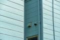 Hidden house nook with exterior vents and pipes in the shadows and slatted wood panels on the outside with a sky blue