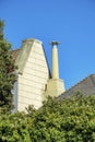 Hidden metal chimney vents with white wooden facade and brown roof with front yard trees and blue sky background