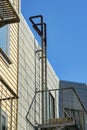 Hidden metal fire escape ladder with beige and light brown wooden pannels and blue sky background near timber home