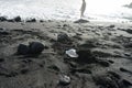 Hidden plastic bottle in the black sand and ignorant teenager tourist in the sea. Disaster in the beach with trash and unhygienic