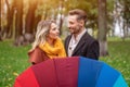 Hiding behind rainbow colored umbrella looking at each others eyes beautiful in love couple standing in the park under a Royalty Free Stock Photo