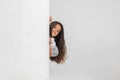 Portrait of little cute smiling Caucasian girl peeking around the corner over white studio background.