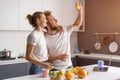 Hiding from a ray of lights shining from a window young couple making breakfast in kitchen at home. Girl hug husband