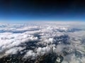 High altitude photograph of the snow covered alps with dark sky and white clouds covering the earth with curved horizon
