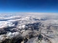 High altitude photograph of the snow covered alps with blue sky and white clouds covering the earth with curved horizon