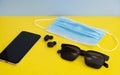 High angel shot of mobile phone, protective mask, earphone and sunglasses on yellow table Royalty Free Stock Photo