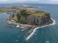 High angle aerial drone view of landmark the Nut, an extinct volcano table mountain, the harbour and the town of Stanley