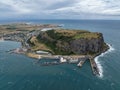 High angle aerial drone view of landmark the Nut, an extinct volcano table mountain, the harbour and the town of Stanley