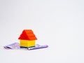 High angle close up shot of a small toy house with money notes below it and white background having copy space Royalty Free Stock Photo