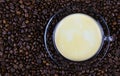 High angle close up view on isolated transparent coffee cup on glass saucer with cafe crema on countless roasted beans background Royalty Free Stock Photo