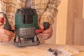 Crop anonymous male carpenter using electric milling machine while cutting wood plank in home workshop Royalty Free Stock Photo