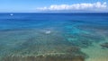 High-angle of Hawaii ocean with reef and sailboat on the horizon clear sunlit sky background