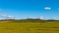 High angle of a large green field with haycocks around, green hill, cloudy, sunlit sky background