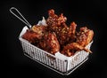 High angle shot of a basket of delicious fried chicken with hot sauce on a black surface