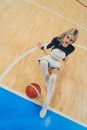 High angle shot of a blond cheerleader sitting on the floor with her hands put also on the floor and a basketball in Royalty Free Stock Photo