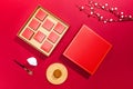 High angle shot of a box of chocolate and some miniature utensils on a red surface