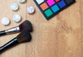 High angle shot of eyeshadow palette, brushes, and silver glosses on a wooden surface