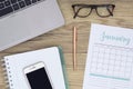 High-angle shot of a home office desk space with a laptop keyboard, phone, notebook, glasses and a calendar with pen