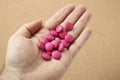 High angle shot of a human's hand with a handful of pink pills, on a pink background