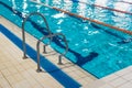 High angle shot of a metal swimming pool ladder with a pool lane in a background.