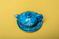 High angle shot of a miniature blue kettle on a yellow surface