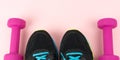 High angle shot of a pair of sports shoes and two pink dumbbells on a pink surface