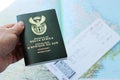 High angle shot of a person holding a passport over a plane ticket and a geographical map
