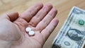 High angle shot of a person holding two pills over a dollar bill on a wooden surface Royalty Free Stock Photo