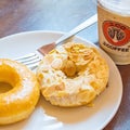 High angle shot of a plate of a plain donut and a peanut donut next to a cup of iced coffee