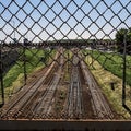 High angle shot of railway tracks through a net surrounded by green grass under beautiful blue sky Royalty Free Stock Photo