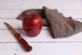 High angle shot of a red apple with a knife, and cloth on a white wooden surface Royalty Free Stock Photo