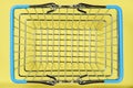 High angle shot of a retail or supermarket empty metal wire shopping basket with blue handles on a yellow background