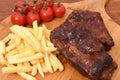 High angle shot of roasted meat on a wooden board with french fries and cherry tomatoes on it Royalty Free Stock Photo