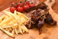 High angle shot of roasted meat on a wooden board with french fries and tomatoes on it Royalty Free Stock Photo