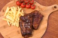 High angle shot of roasted meat on a wooden board with french fries and tomatoes on it Royalty Free Stock Photo