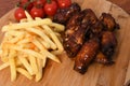 High angle shot of saucy chicken wings, french fries, and tomatoes on a kitchen board Royalty Free Stock Photo