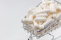 High angle shot of a small shopping cart full of white pills. White background, copy space. Close up shot. Shopping online, buying Royalty Free Stock Photo