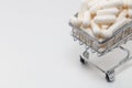 High angle shot of a small shopping cart full of white pills. White background, copy space. Close up shot. Shopping online, buying Royalty Free Stock Photo