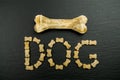 High angle shot some dog food shaped like the word Dog` and a chew bone on a black surface`